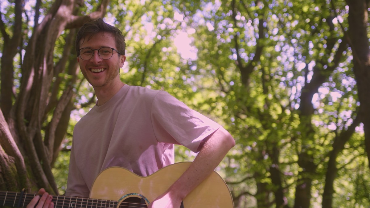 Matthew Annable holding an acoustic guitar in woodland