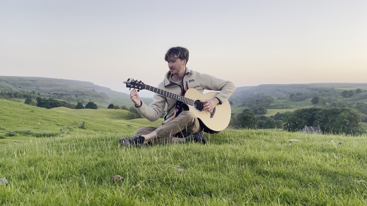 Matthew playing guitar sitting in a Yorkshire field at dusk