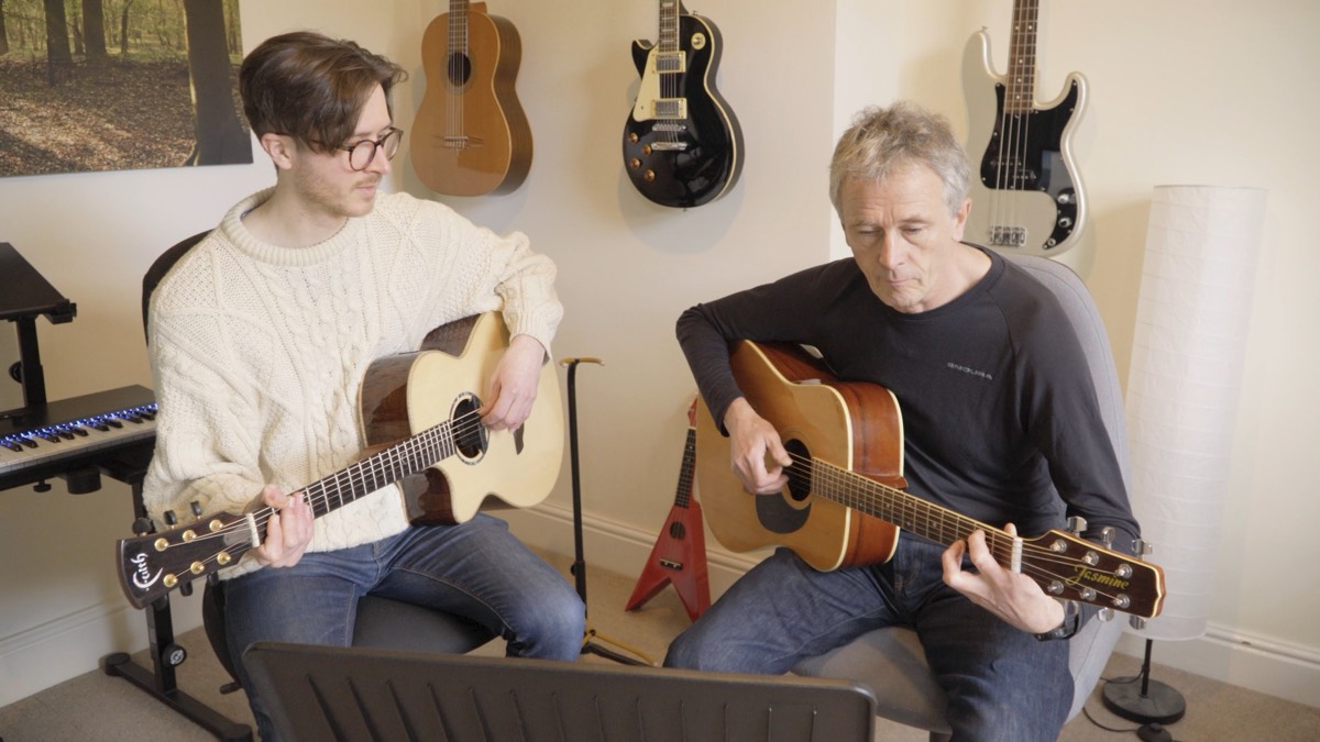 Matthew teaching an adult student, both playing acoustic guitars